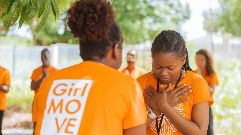 A young woman from the Girl MOVE Academy Leadership and Social Innovation Program stands before another woman, bowing her head and crossing her hands on her chest.